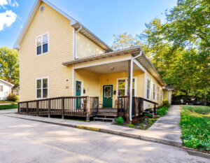 Yellow building with green doors and windows with white trim with a wheel chair ramp.